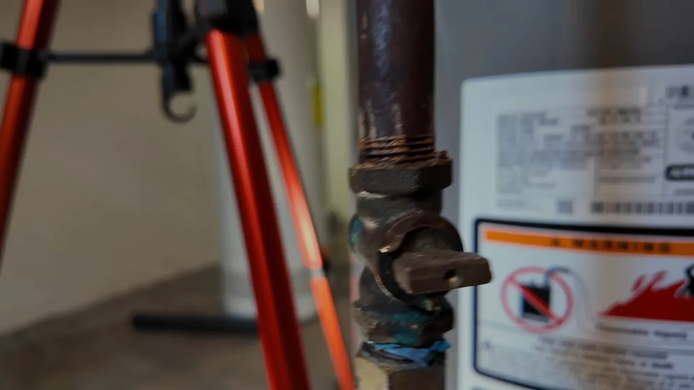 Black iron gas pipe with a shutoff valve handle beside the label on a water heater
