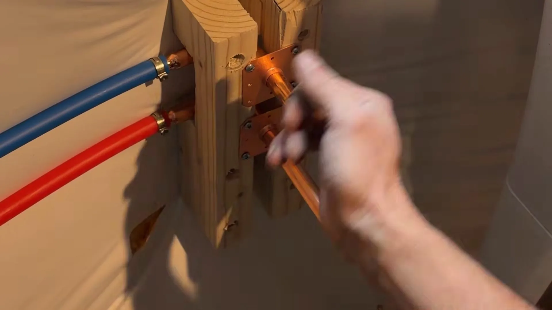 Hand fitting a copper stub-out to a wood frame while blue and red PEX lines run alongside
