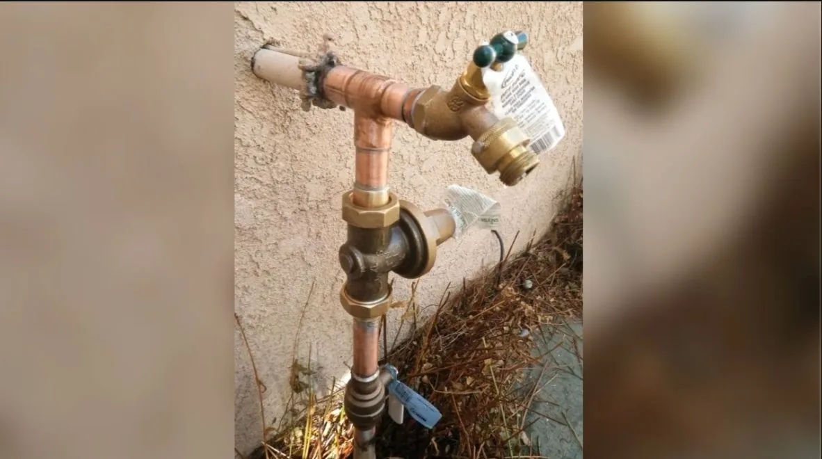 Outdoor brass spigot with a green handle and a shutoff valve below it on a stucco wall