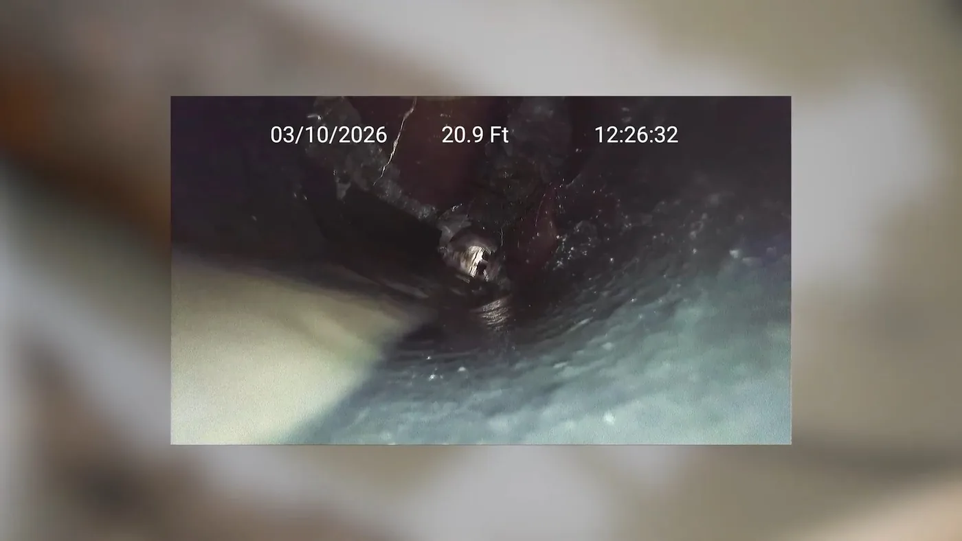 Small camera monitor screen showing a dark, rough pipe interior with a date and distance readout