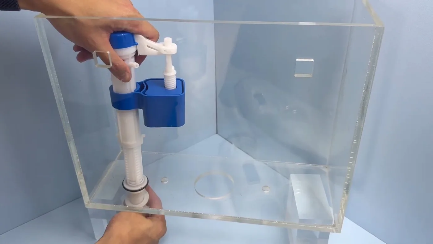 Hands holding a clear acrylic tank that shows a blue toilet fill valve inside it