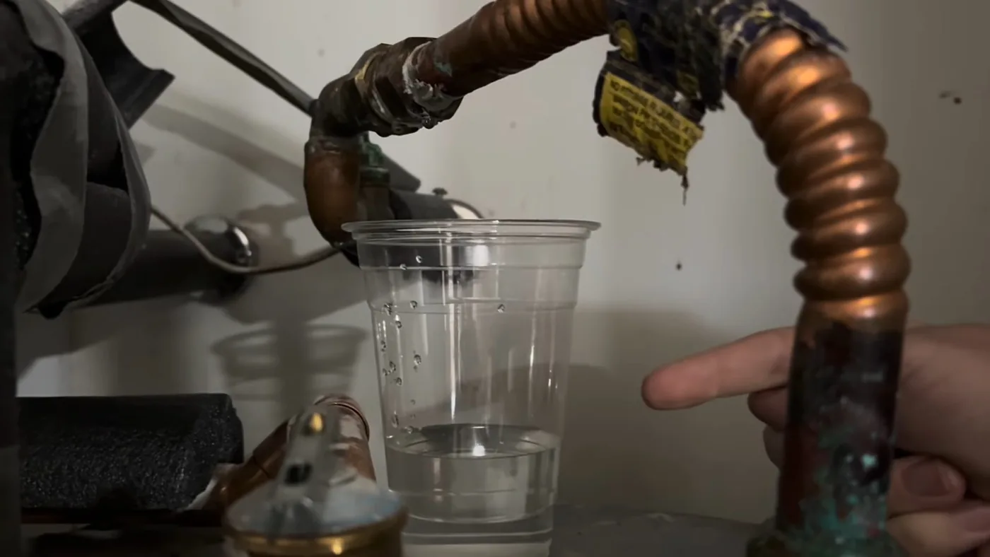 Clear plastic cup held under a copper line while a finger points at the valve above it