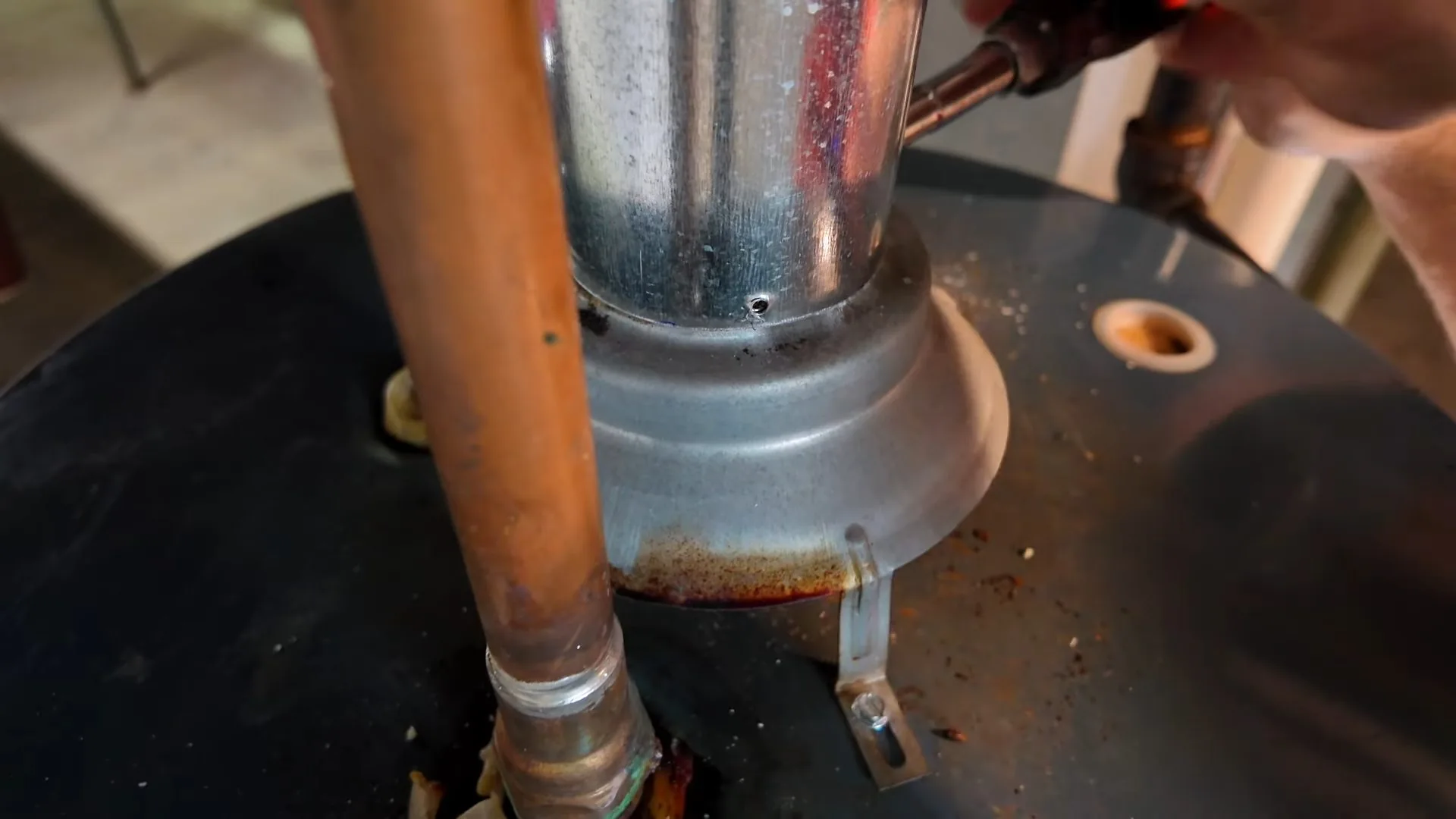 Copper pipe and a galvanized vent collar on the top of a black water heater tank