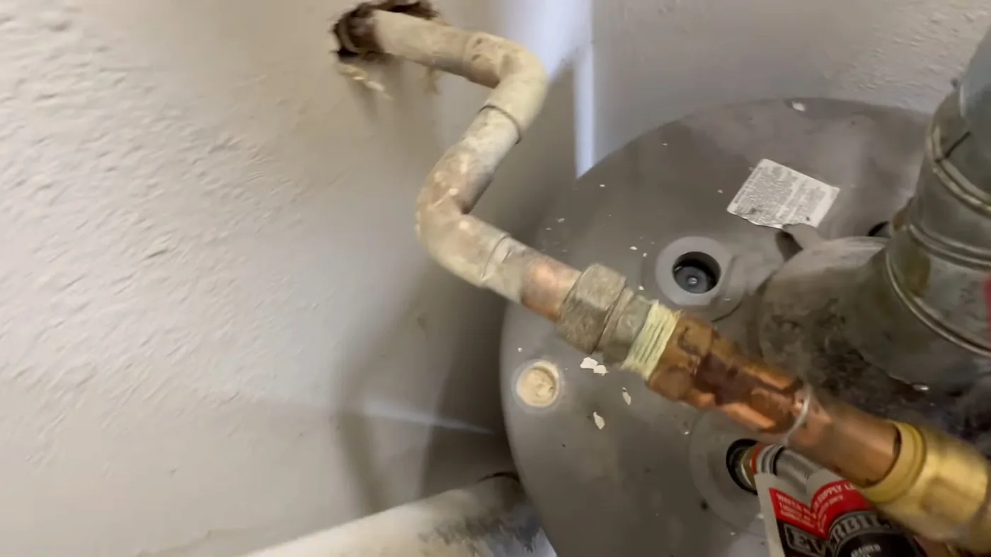 Top of a gray water heater tank with copper pipes, a flexible connector and a metal vent collar