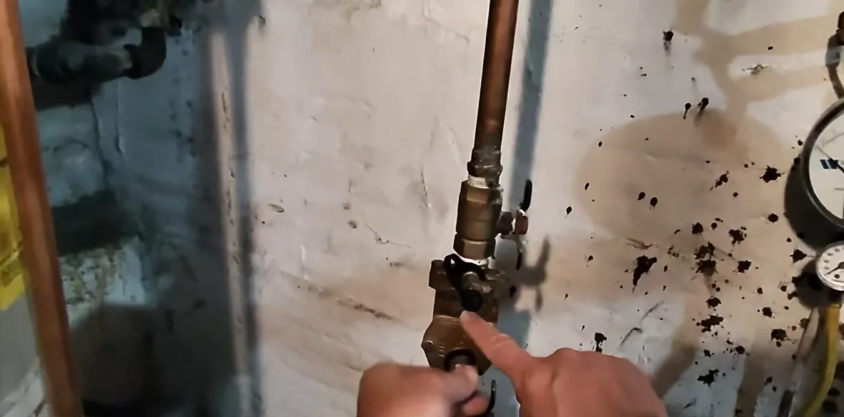 Hand on a brass shutoff valve on a basement wall, with dark specks splattered across the paint