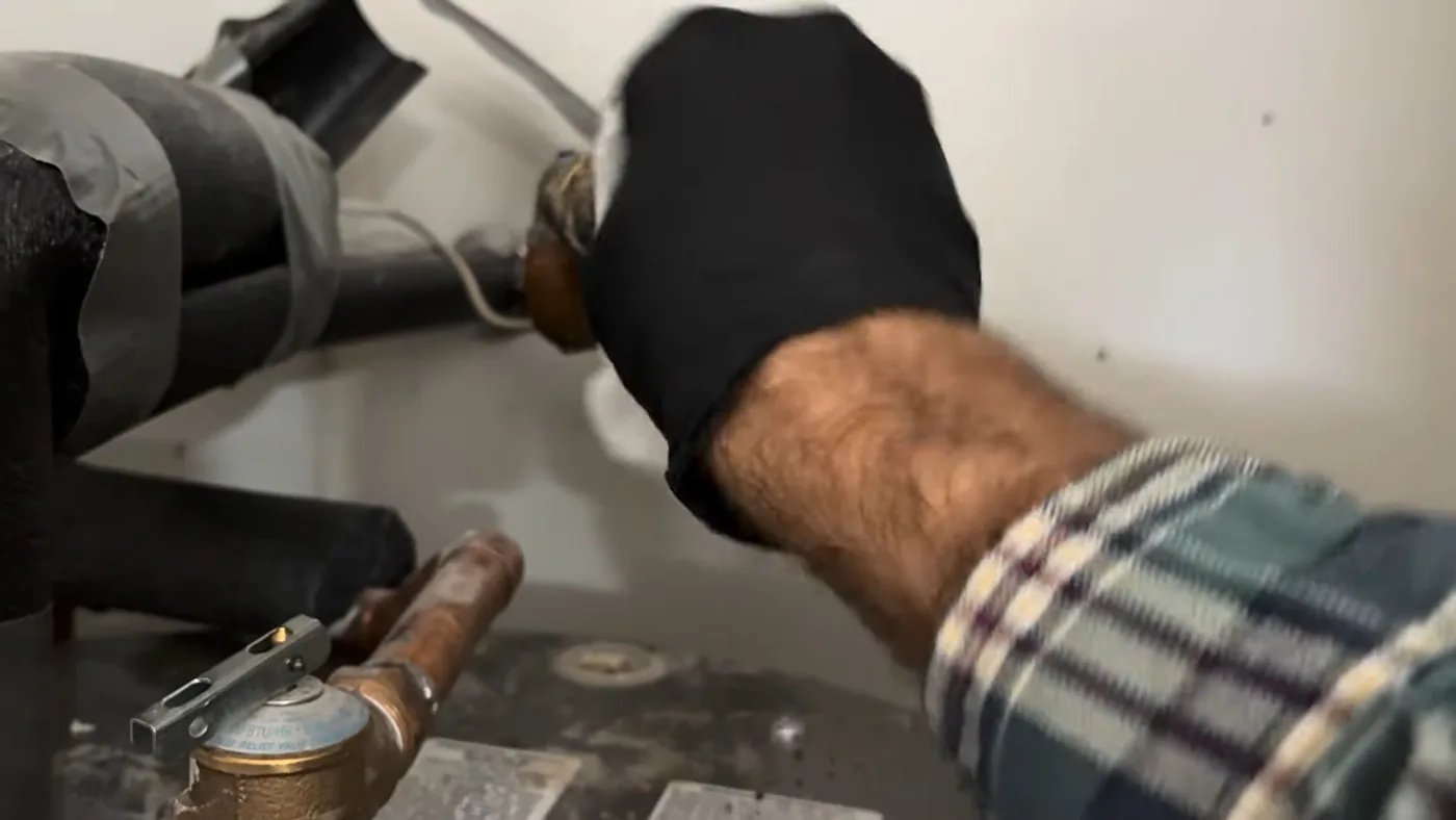 Gloved hand resting on black foam-insulated pipes beside a water heater