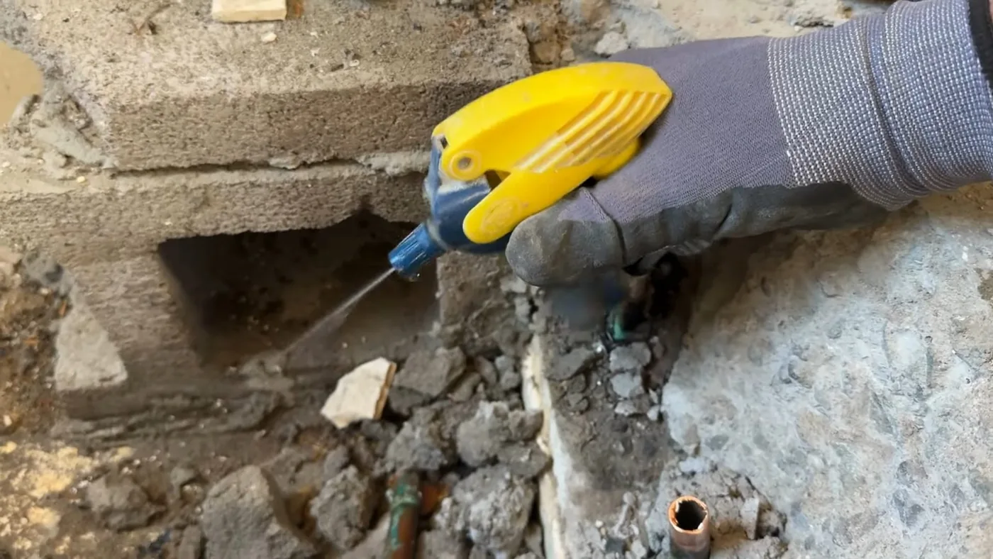 Gloved hand holding a small chisel against broken concrete with a copper line showing nearby