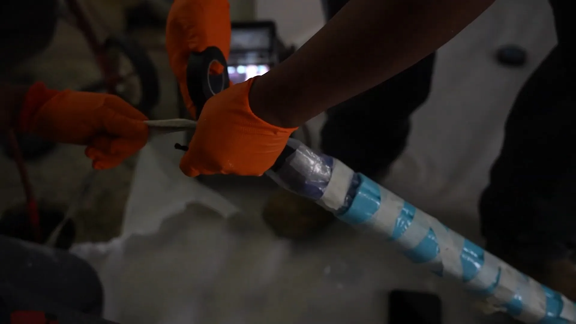 Gloved hands wrapping blue and white liner material around a length of pipe