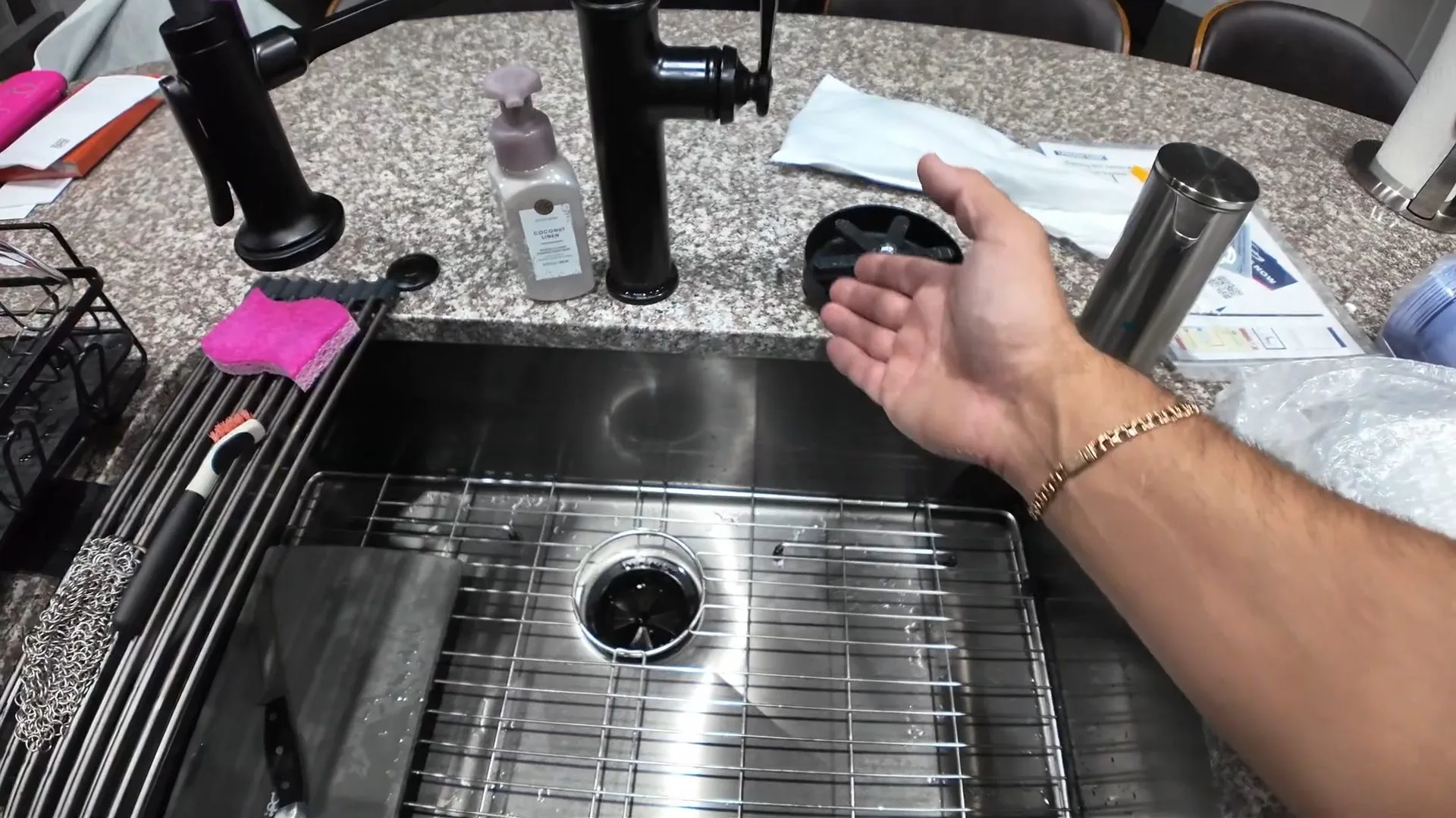 Hand resting above a stainless steel sink with a round drain opening at the center of the basin