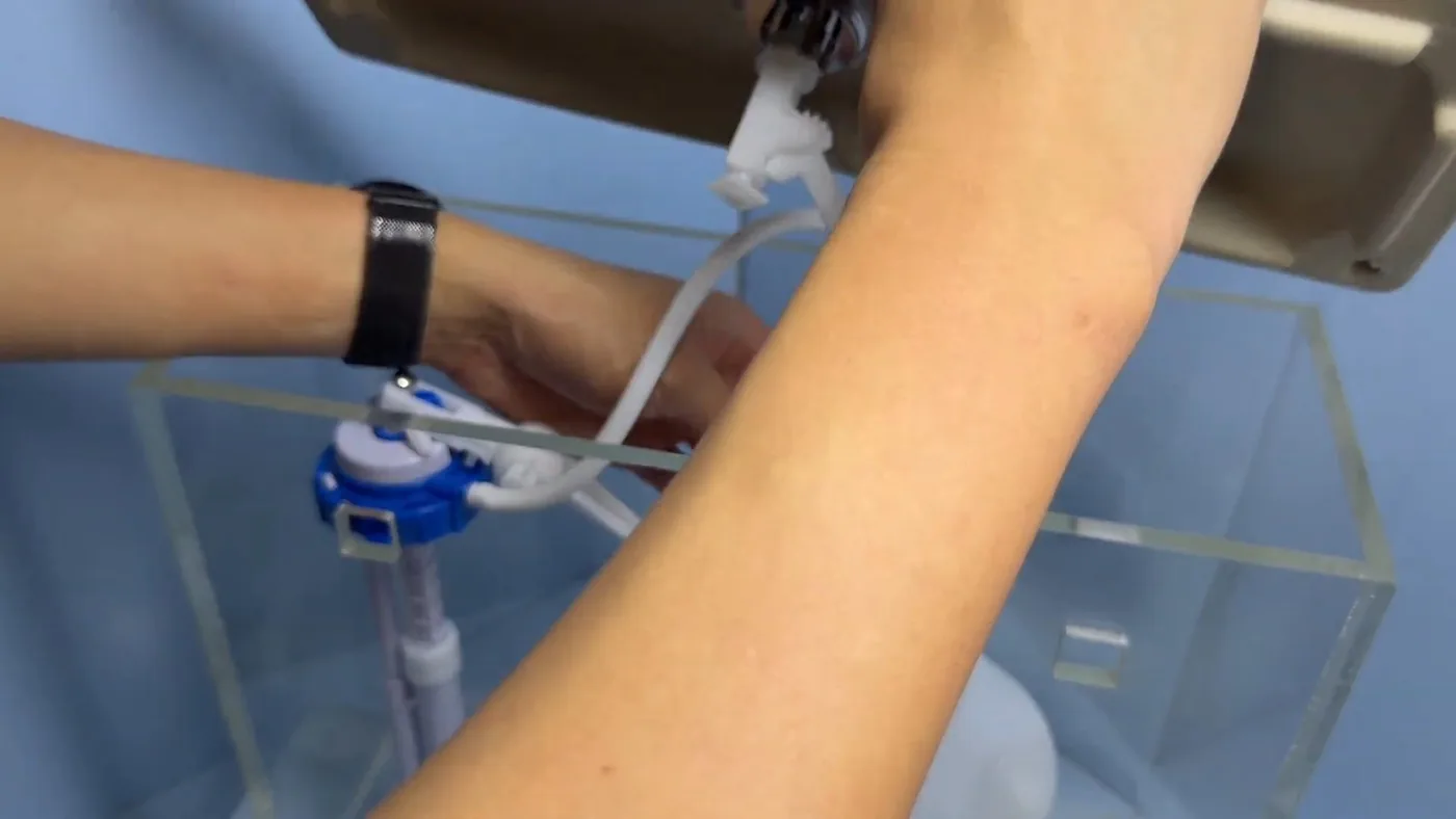 Hand adjusting a plastic fill valve inside a clear tank with water supply tubing
