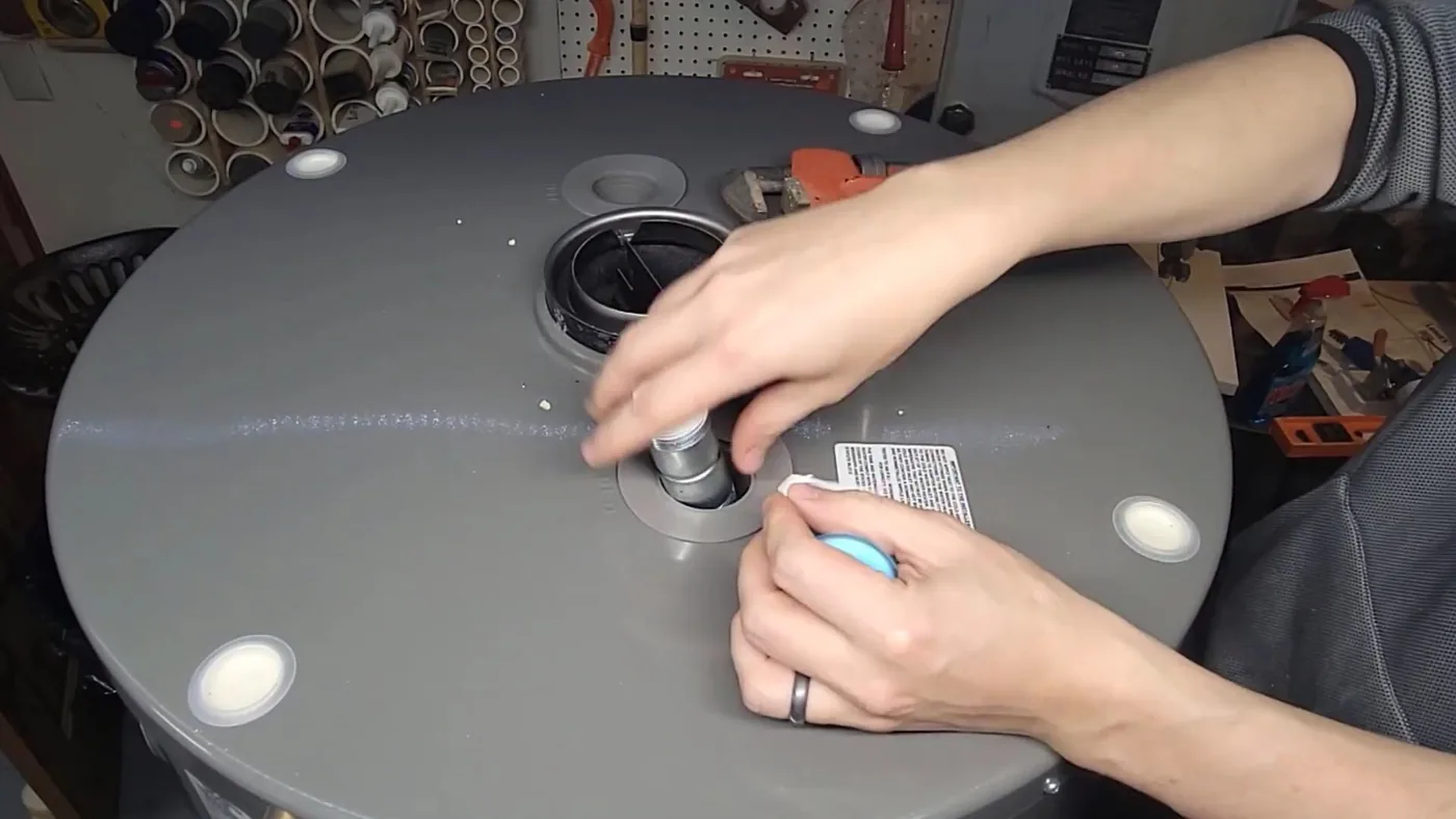 Hands tightening a fitting on top of a gray water heater tank