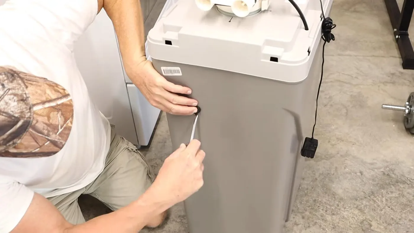 Man in a cap using a small tool to open the cover of a gray water softener