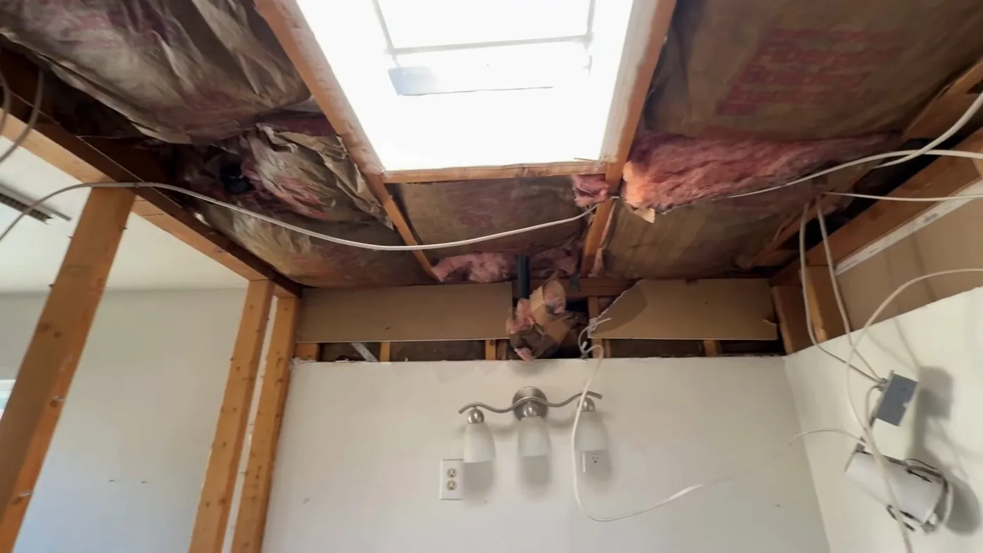 Opened ceiling in a bathroom with exposed joists, pink insulation and a skylight