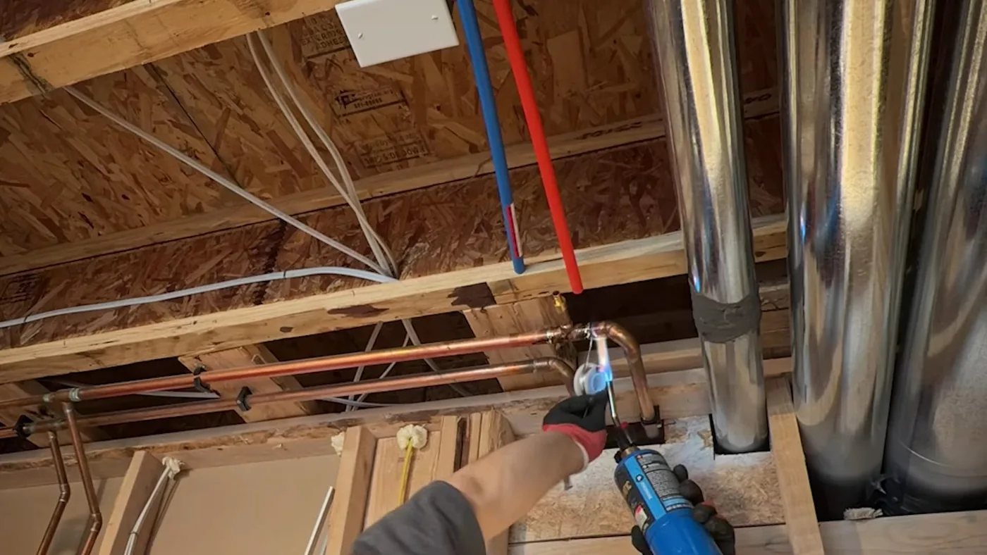 Blue and red PEX lines and copper pipes running through open floor joists beside metal ductwork