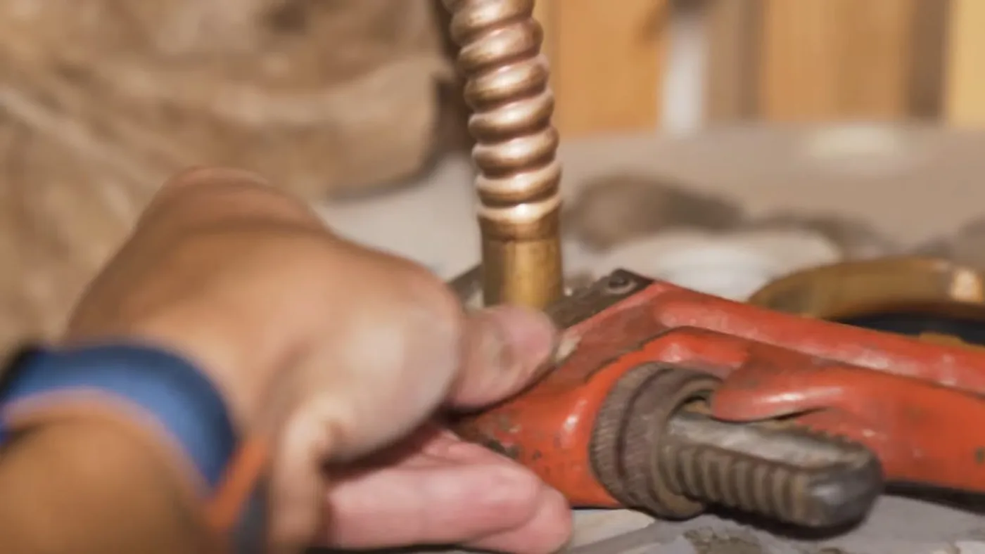 Hand holding a pipe wrench on a copper tube above a water heater