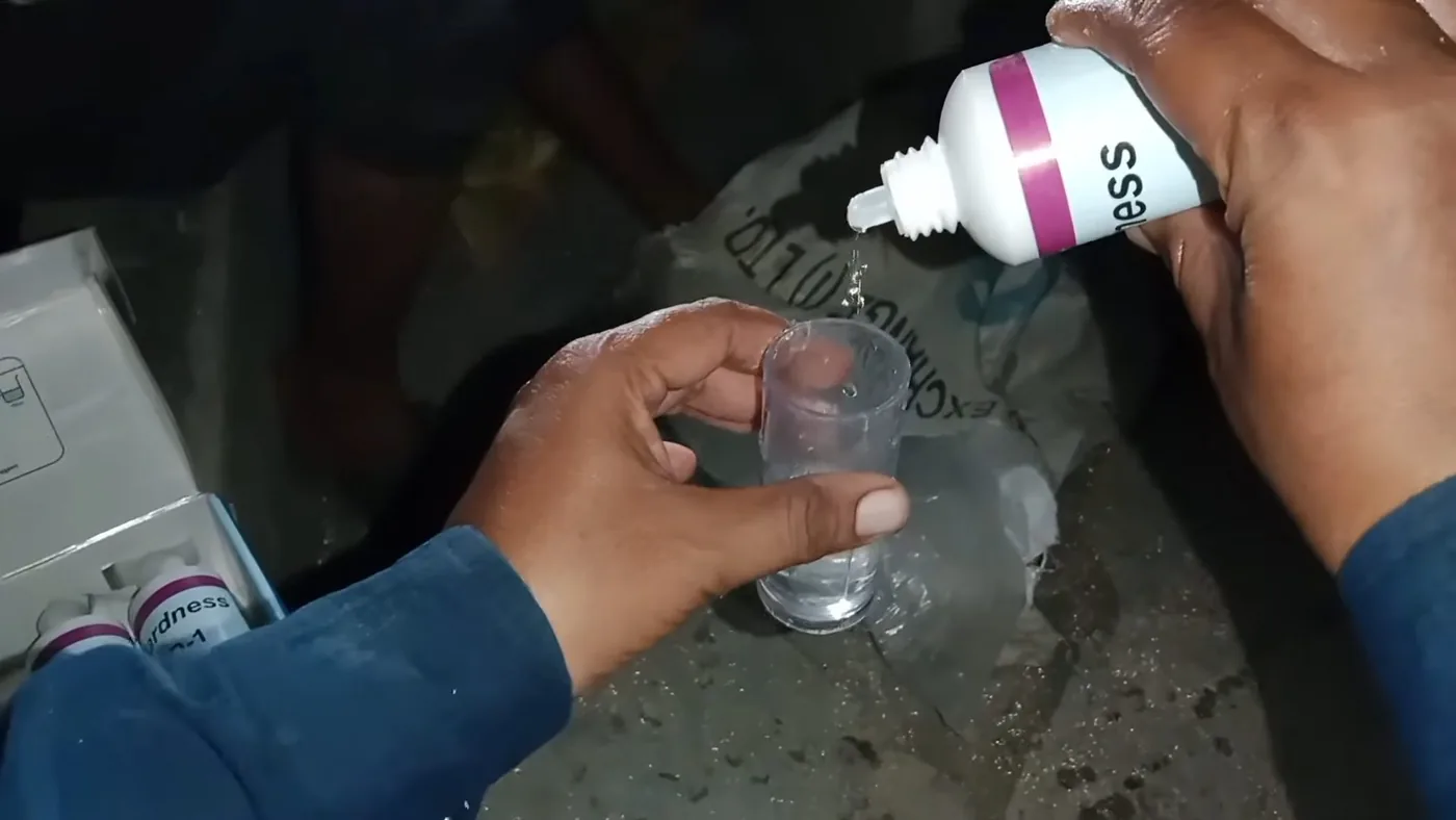 Hands squeezing drops of reagent from a small bottle into a glass of water