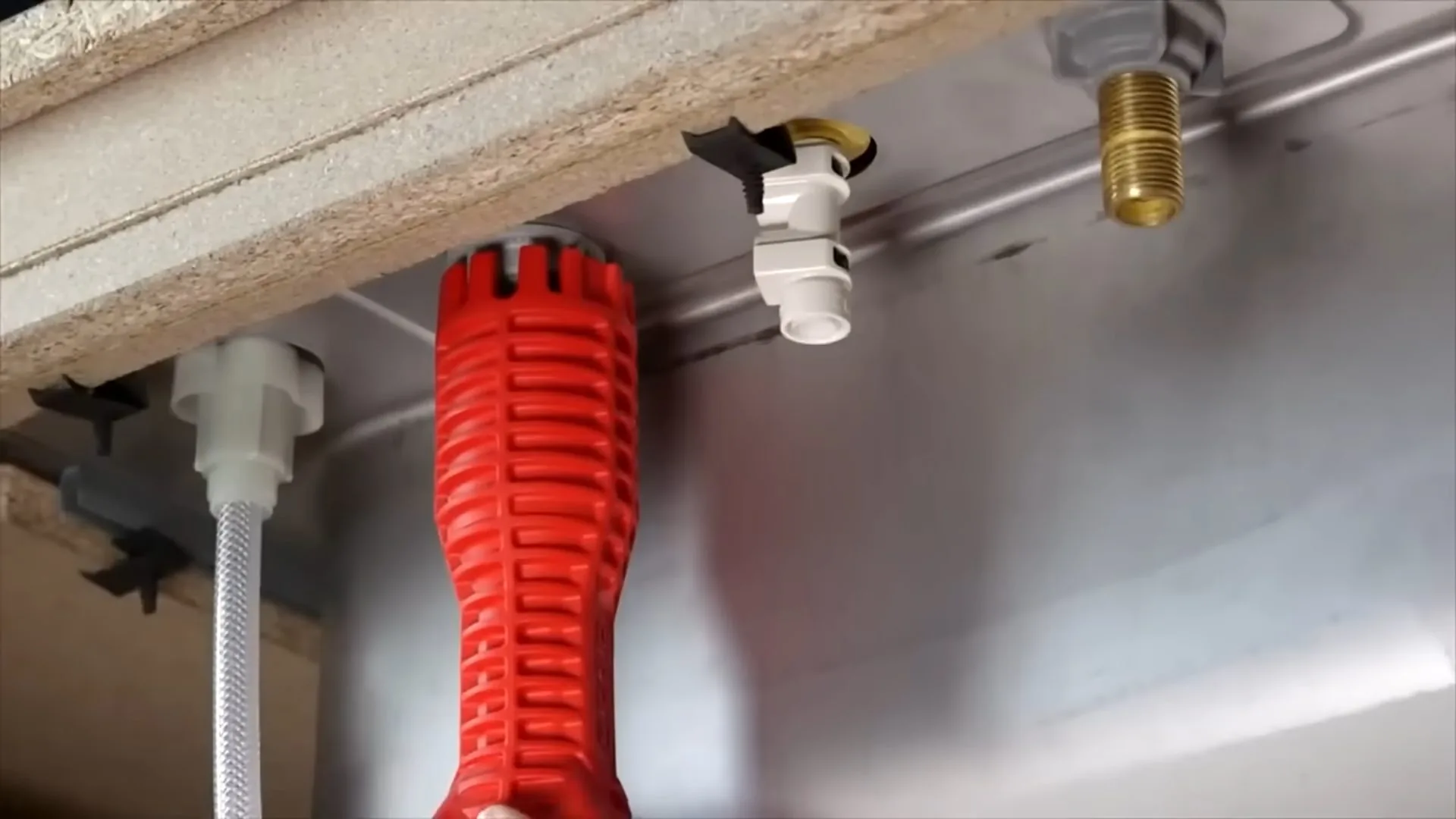 Red basin wrench reaching up to the supply fittings beneath a stainless steel sink