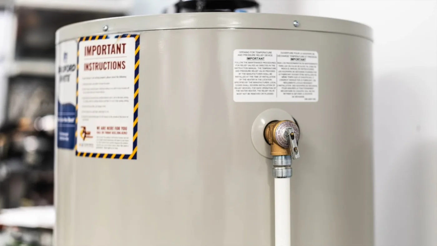 Relief valve on the side of a tank water heater with a white discharge pipe running down from it