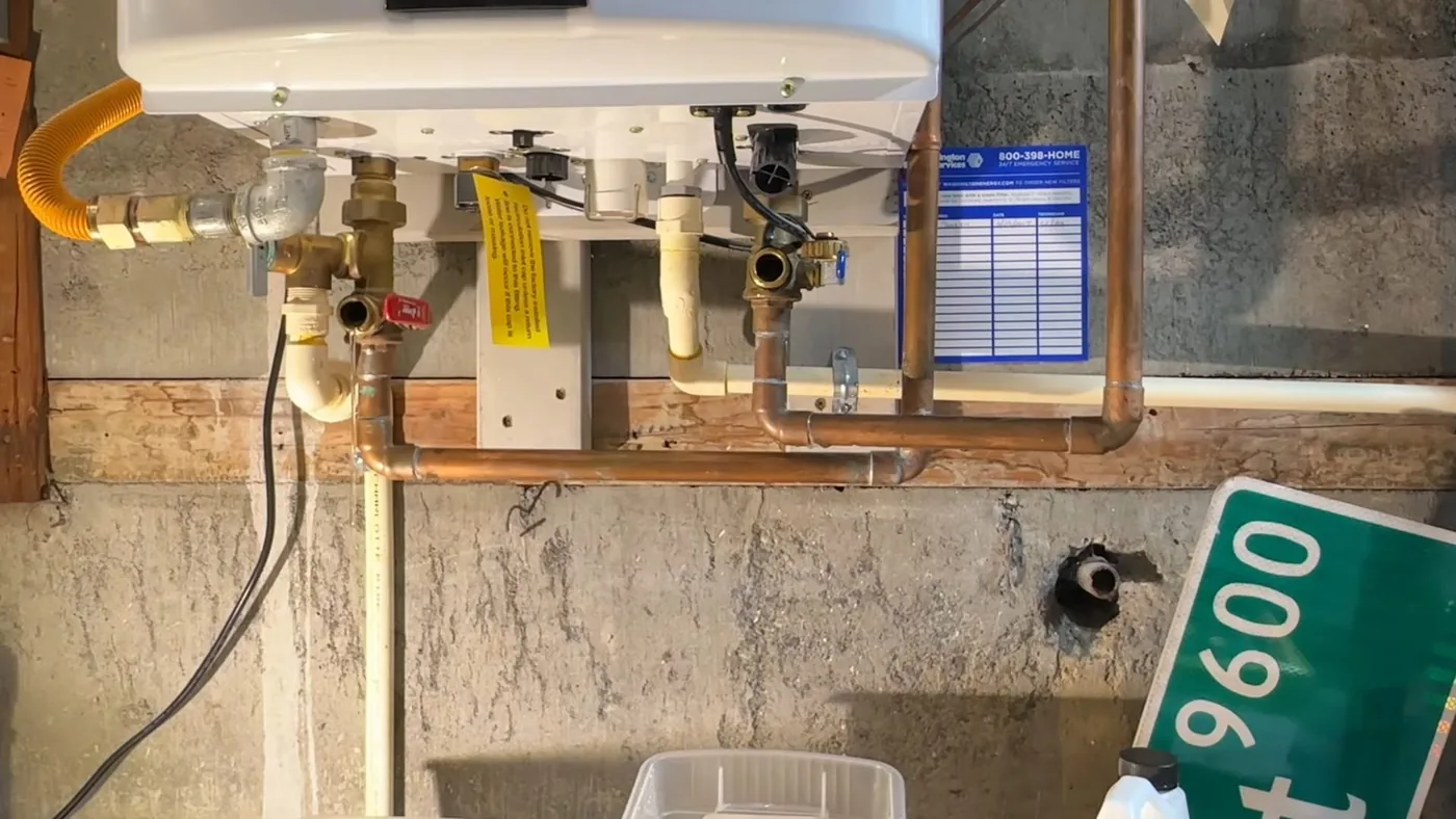 Tankless water heater on a basement wall with service valves, copper lines and a gas connection beneath it