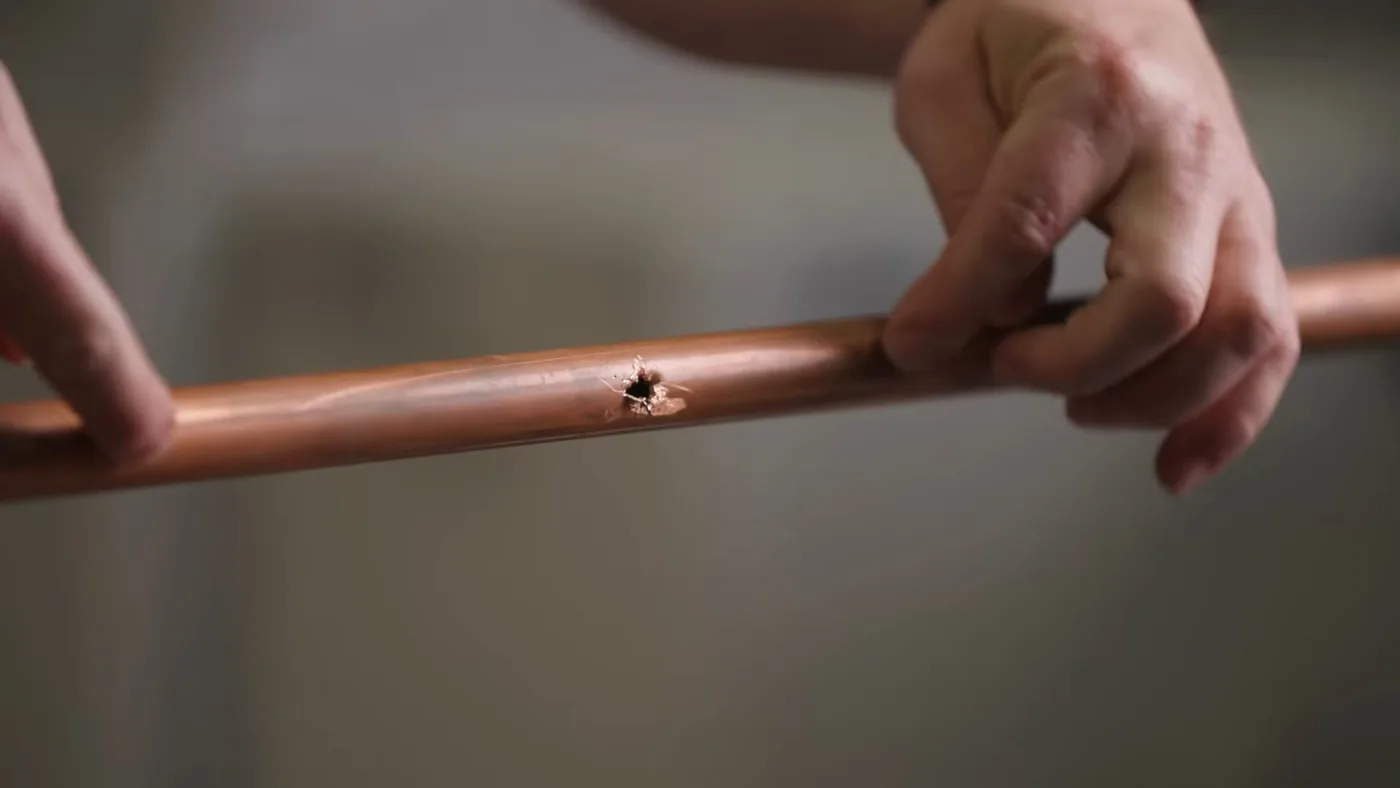 Hands holding a length of copper pipe with a small hole in its side
