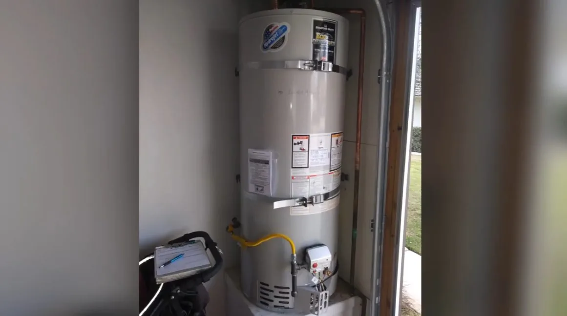 Tank water heater standing in a narrow utility closet with a gas line at its base