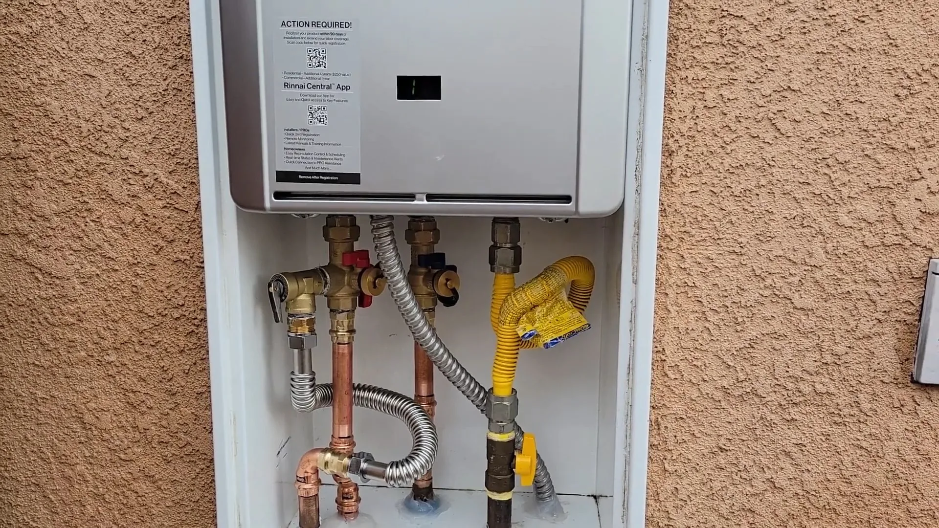 Wall-mounted tankless water heater in a recessed cabinet, with a set of valves and a gas line below it