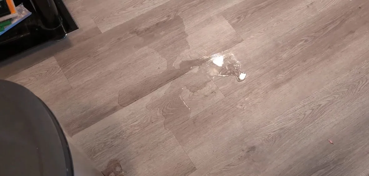Small puddle and droplets of water on a gray plank floor