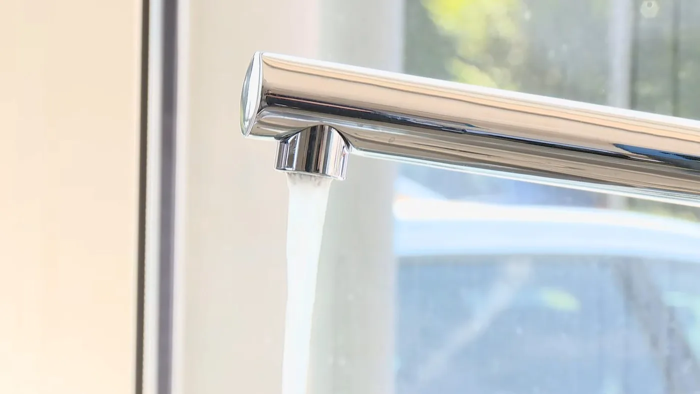 Water running from a chrome faucet spout beside a window
