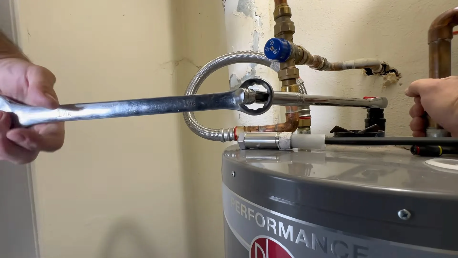 Wrench held against a flexible connector at the top of a gray tank water heater