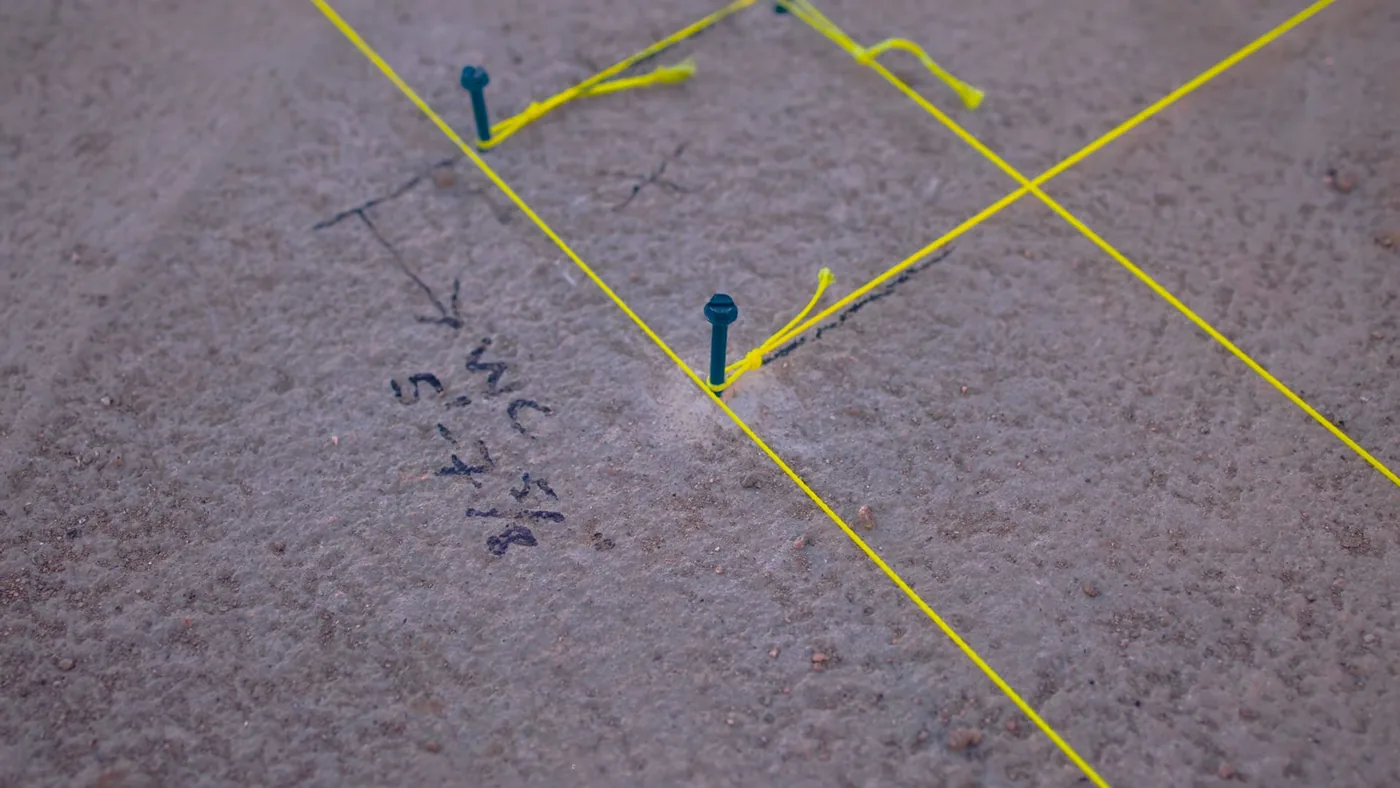 Yellow flags and hand-written paint marks on bare ground showing where buried lines were marked